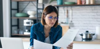 young woman working with computer while consulting some invoices and documents in the kitchen