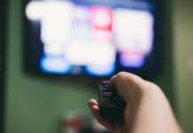 JustWatch svela i contenuti streaming più seguiti del 2025 in Italia Woman using remote to search for movies on the television